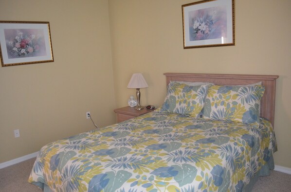 A bedroom with a floral bedspread, a bedside lamp, and two framed floral artworks on the walls.
