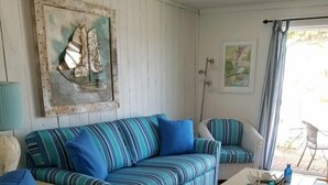 Ein gemütliches Wohnzimmer mit gestreiften blauen Sofas, einem weißen Couchtisch und einer rustikalen Holzbalkendecke.