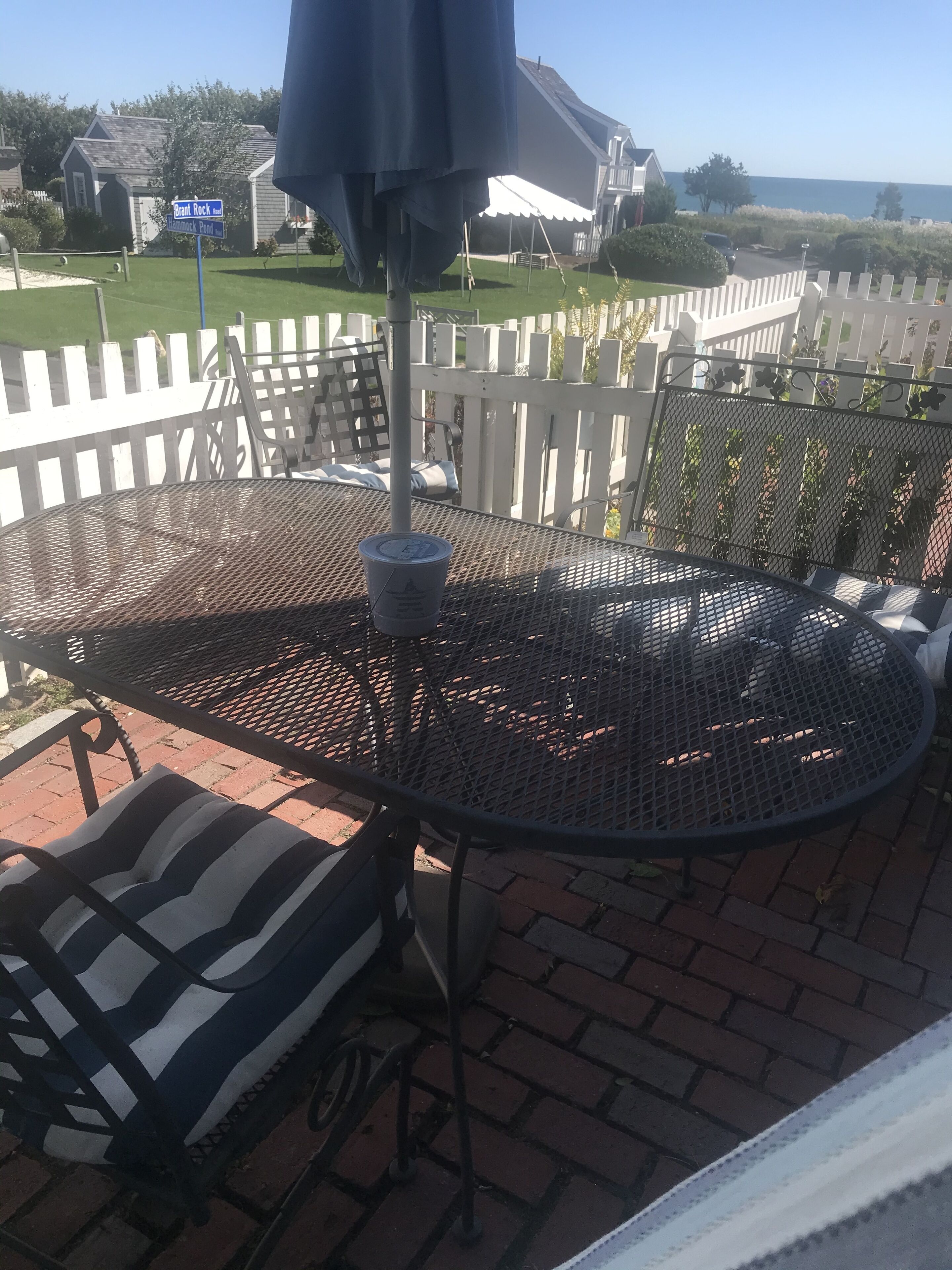 A patio with a round metal table, a striped cushion, and a white picket fence.