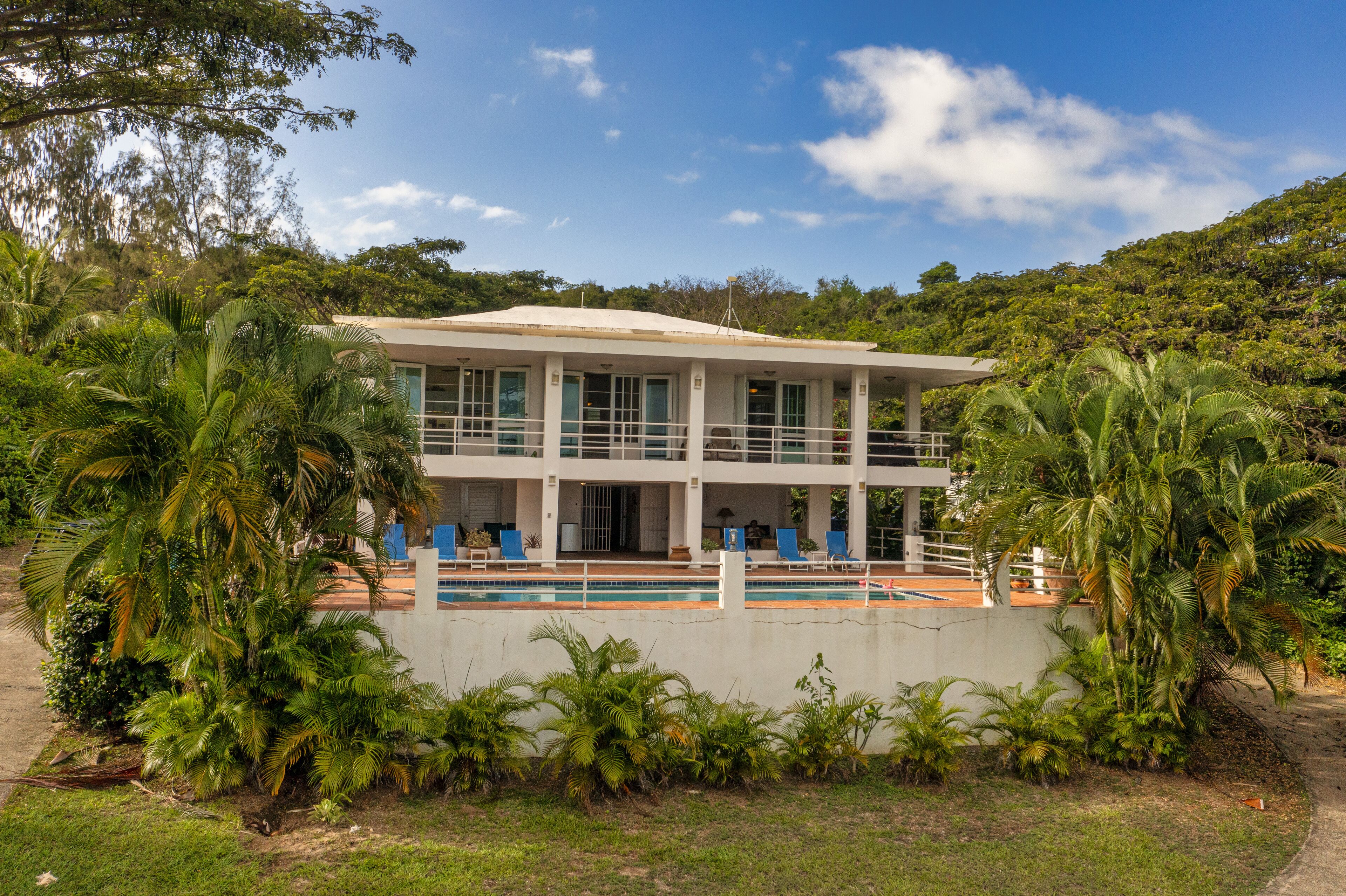 A two-story building with a pool, surrounded by lush greenery and palm trees.