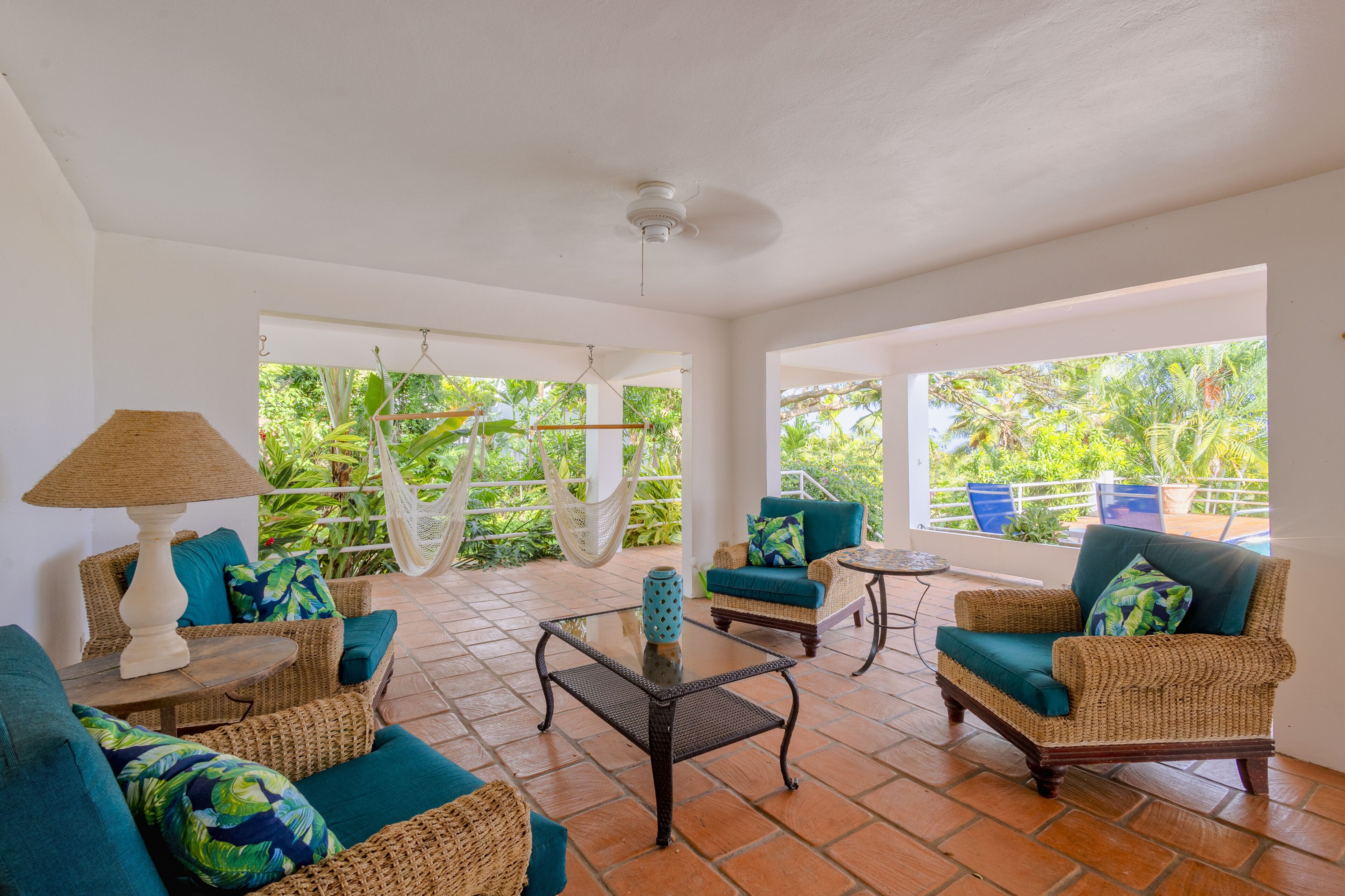 A spacious patio with wicker furniture, a glass coffee table, and a hammock.