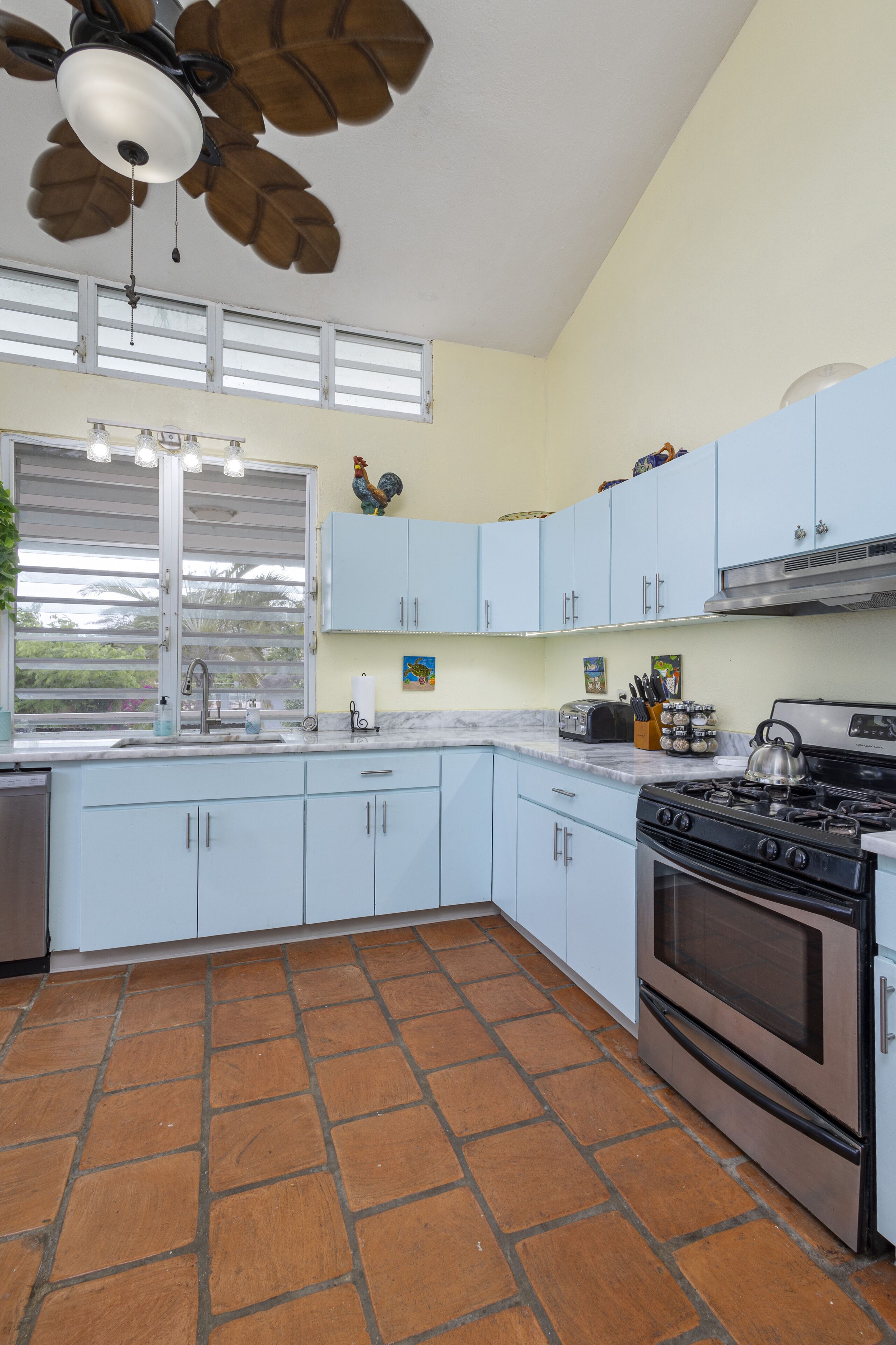 A kitchen with light blue cabinets, a stove, a sink, and a ceiling fan.