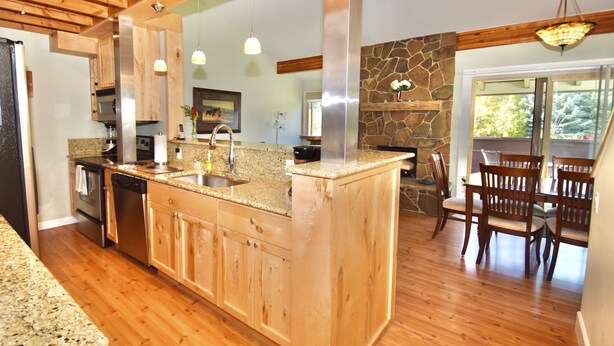 Une cuisine moderne dotée de plans de travail en granit, d’armoires en bois, d’un grand îlot central et d’un mur d’accent en pierre.