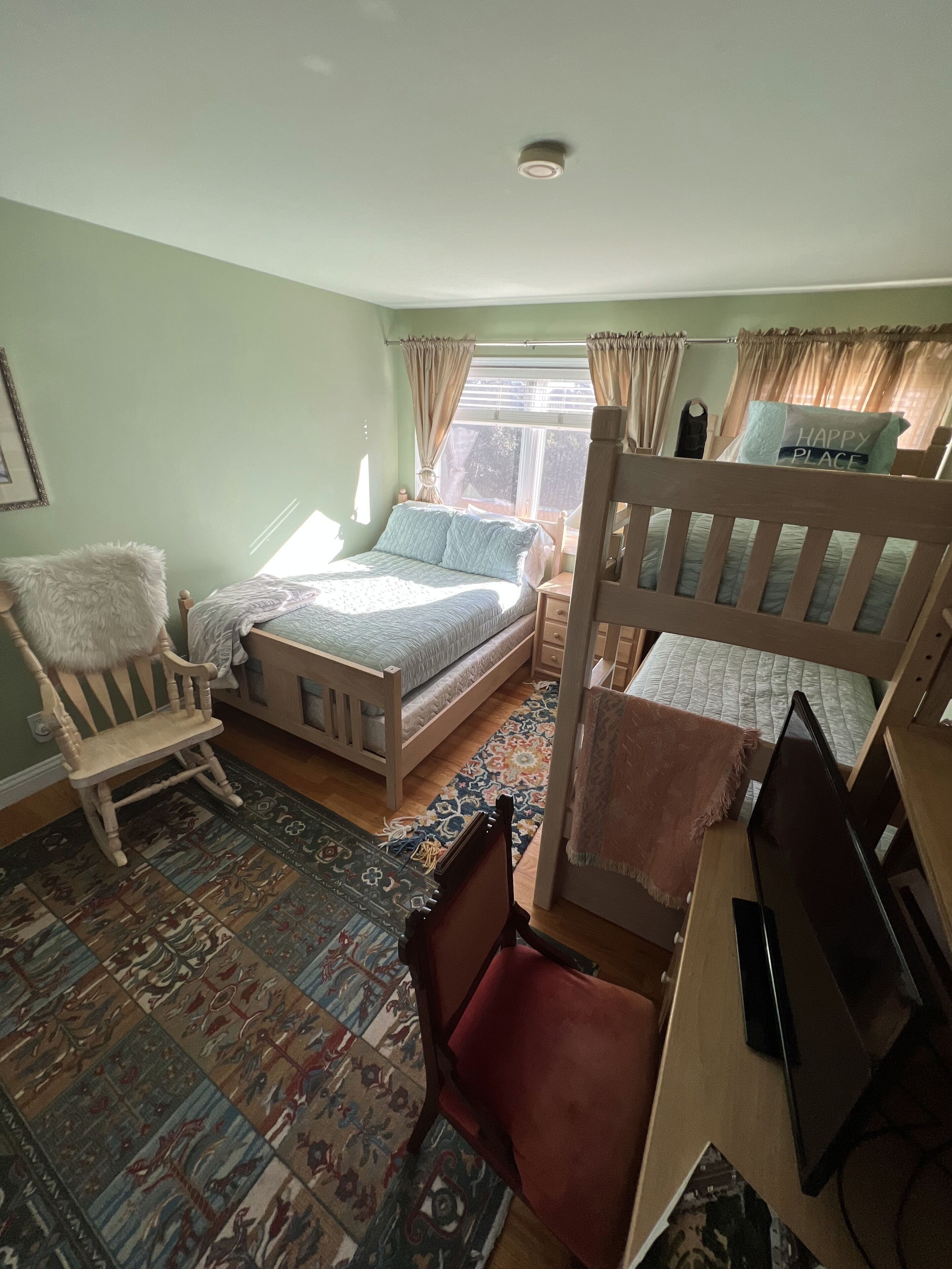 A bedroom with two beds, a chair, a desk, and a large window.
