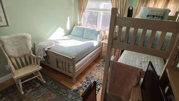 A bedroom with two beds, a chair, a desk, and a large window.