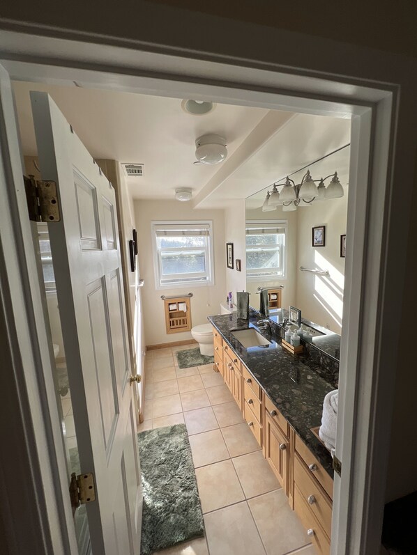 A kitchen with a marble countertop, wooden cabinets, a sink, and a window with blinds.
