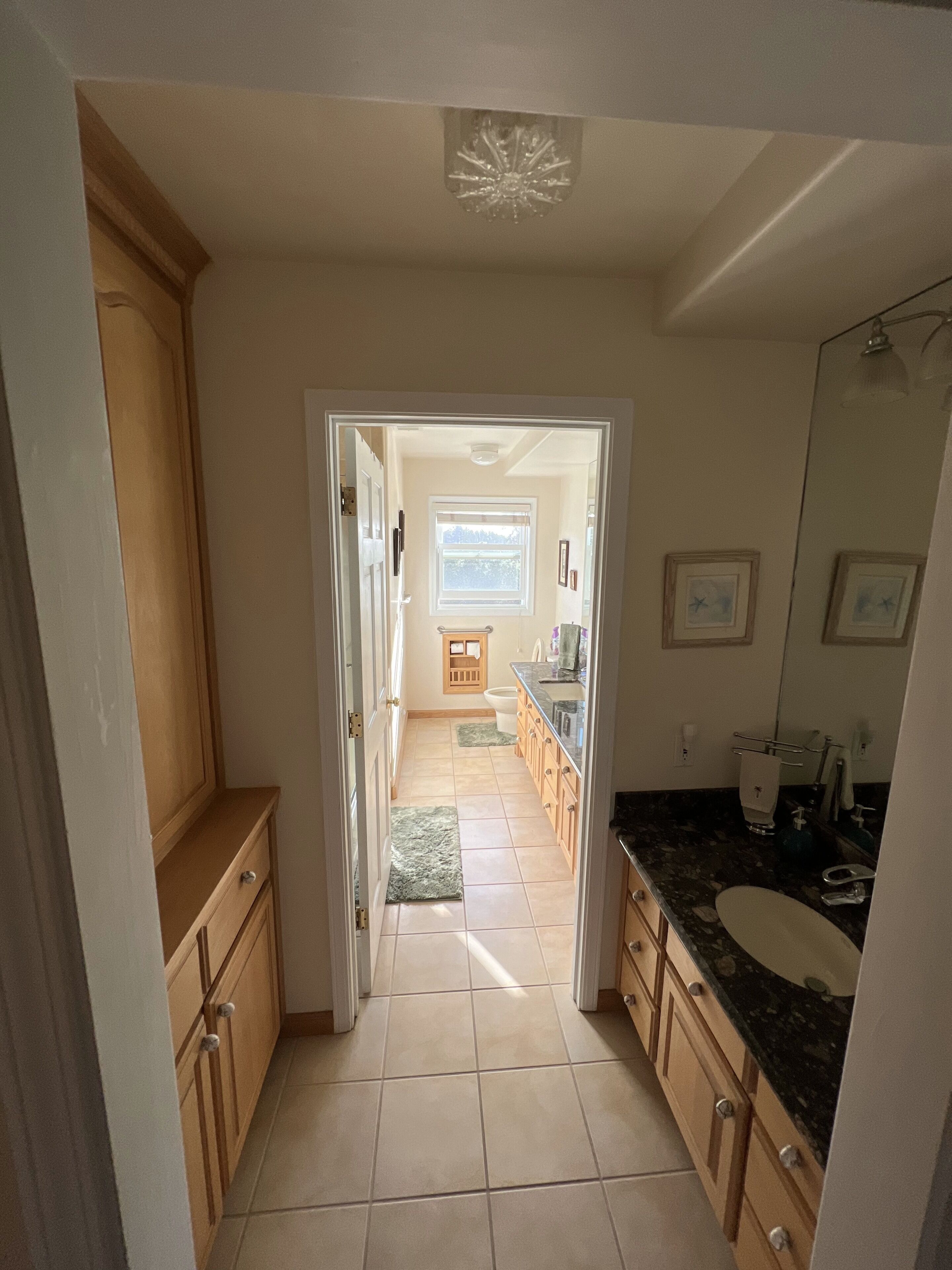 A narrow hallway leading to a bathroom with a sink, mirror, and window.