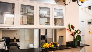 Eine Küche mit weißen Schränken, einem Edelstahl-Kühlschrank, einer Obstschale auf der Arbeitsfläche und einer Vase mit Blumen.