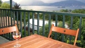 Una mesa de madera con una copa de vino tinto en un balcón con vistas al agua y a las montañas.