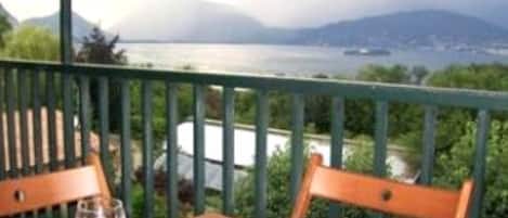 A wooden table with a glass of red wine on a balcony overlooking a body of water and mountains.