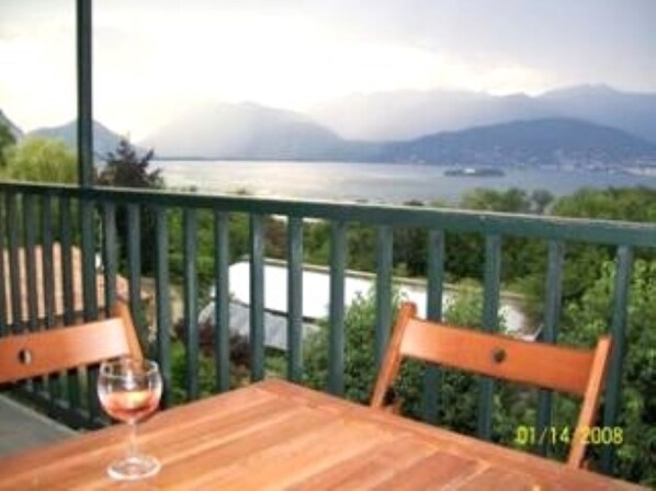 A wooden table with a glass of red wine on a balcony overlooking a body of water and mountains. - On Top Of The Lake With Views Of The Lake & The Swiss Alps (Stresa)