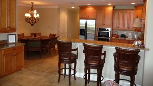 A kitchen with wooden cabinets, a granite countertop, a stainless steel refrigerator, an oven, and a chandelier. - Luxurious, peaceful beachfront condo minutes from St Augustine and Daytona Beach (Beverly Beach)