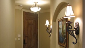 A hallway with a wooden door, a round rug, a painting on the wall, and wall-mounted lamps. - Luxurious, peaceful beachfront condo minutes from St Augustine and Daytona Beach (Beverly Beach)