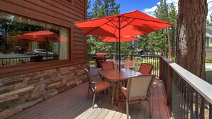 Una terraza de madera con un muro de piedra, mobiliario exterior y sombrillas rojas.