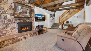 Una sala de estar acogedora con chimenea de piedra, un sofá cómodo y una escalera de madera.