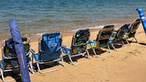 Sillas de playa alineadas en una orilla arenosa con una masa de agua y montañas lejanas al fondo.