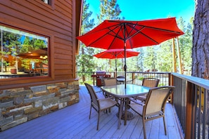 A wooden deck with a stone wall, a glass table with chairs, and a red umbrella.