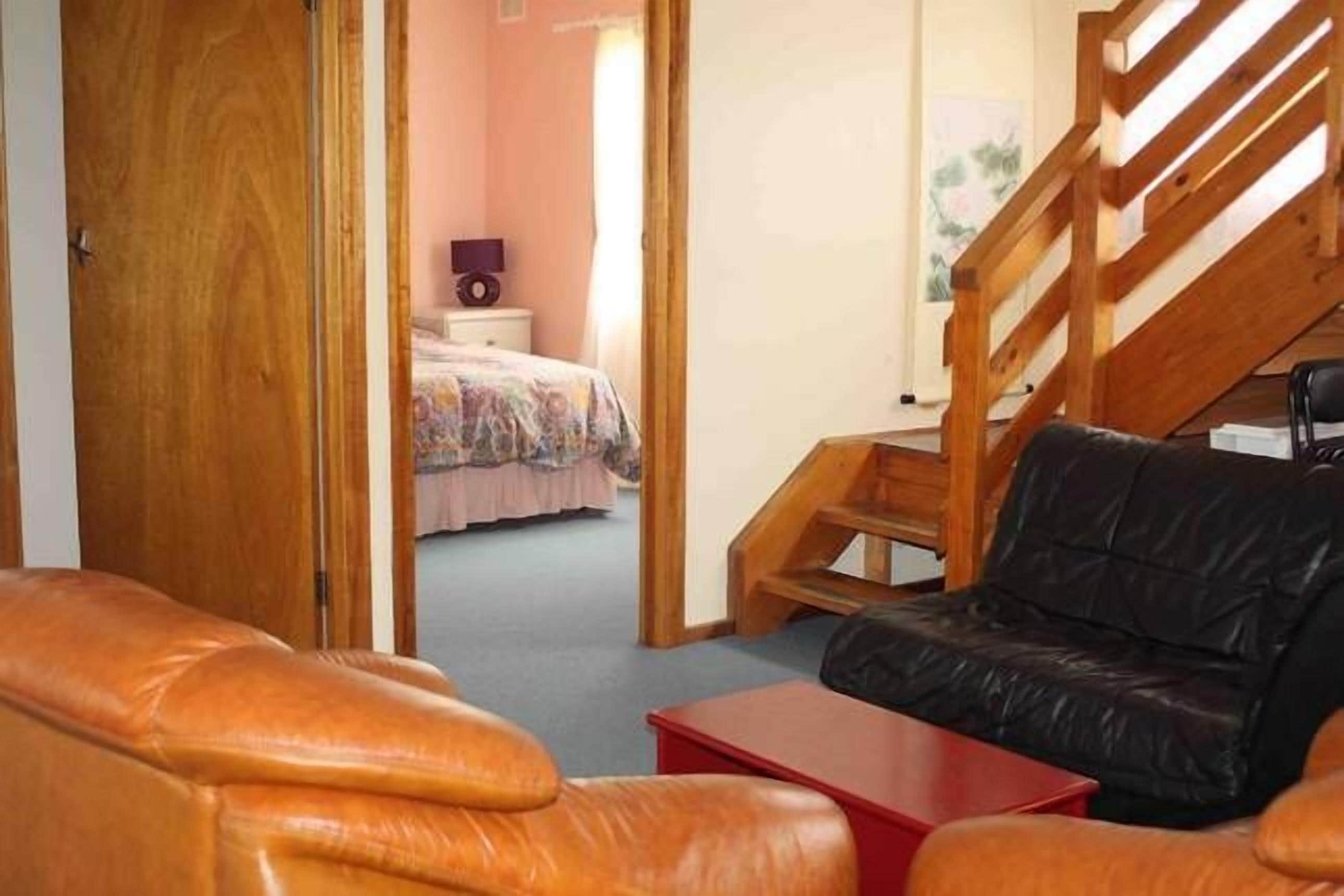 A room with a wooden staircase, a black leather sofa, and a red table.
