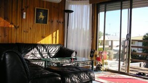Et værelse med en sort lædersofa, et glasbord, et hvidt gardin og udsigt til bygninger gennem en glasdør.