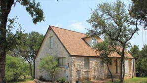 A stone house with a tiled roof, surrounded by trees and a grassy area. - 4/2 by Marina, Near Wineries, Grill, WiFi, View (Spicewood)