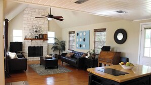 A spacious living room with a stone fireplace, a ceiling fan, a black leather sofa, a wooden coffee table, and a dining area with a wooden table and chairs. - 4/2 by Marina, Near Wineries, Grill, WiFi, View (Spicewood)