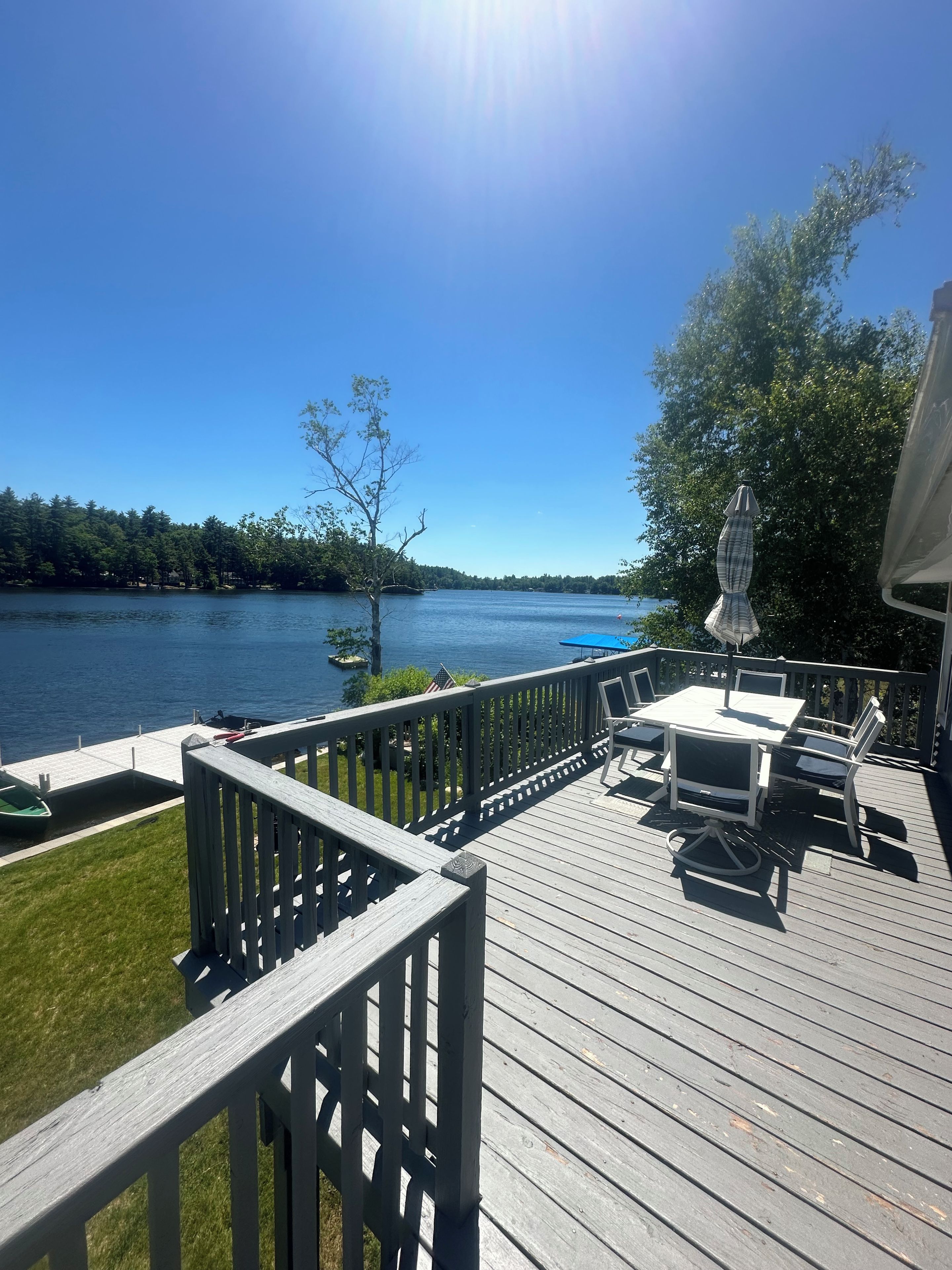 Une terrasse avec une table et des chaises, donnant sur un lac où se trouvent un quai et un bateau.