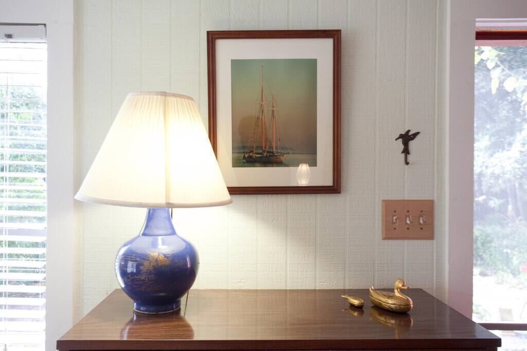 A table with a blue lamp, a framed painting of a sailboat, and two golden swan figurines.