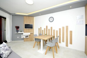 Una sala de estar moderna con comedor, que incluye una mesa de madera, sillas grises, un televisor de pantalla plana y un panel decorativo en la pared.