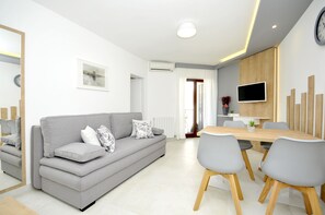 Una sala moderna con un sofá gris, una mesa de comedor con sillas, un televisor de pantalla plana montado en la pared y un mueble de madera.