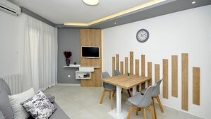 Un salon moderne comprenant un canapé, une table à manger avec des chaises, un téléviseur à écran plat et une horloge murale.