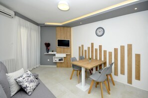 Una sala moderna con un sofá, una mesa de comedor con sillas, un televisor de pantalla plana y un reloj de pared.