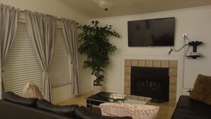 Una sala de estar con chimenea, un televisor montado encima y una planta grande.