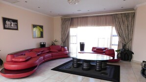 A modern living room with a curved red sofa, a glass coffee table, and a view of the outdoors through large windows.