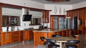 A modern kitchen with wooden cabinets, a large island with seating, stainless steel appliances, and a flat-screen TV mounted above the island.