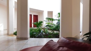A spacious indoor area with a view of a courtyard featuring a red door and lush greenery.