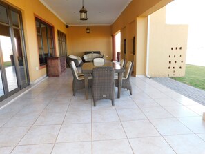 A covered patio area with a dining table and chairs, a trash bin, and a view of the outdoors.