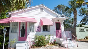 A white house with pink accents, including a door, windows, and awning.