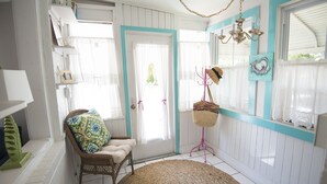 A room with a wicker chair, a round rug, a wicker basket on a pink stand, and a door with a teal frame.