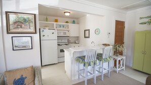 A compact kitchen with white cabinetry, a white refrigerator, a microwave, and a stove. There is a small island with two chairs and a vase of flowers.