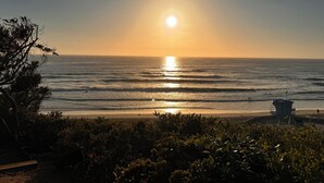 Ein Strand mit Sonnenuntergang über dem Meer, Wellen und einem Rettungsturm.