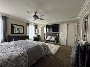 Ein Hotelzimmer mit einem großen Bett, einem Deckenventilator, einem an der Wand montierten Fernseher, einem Sessel und einem Kleiderschrank.