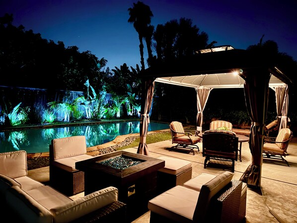 A poolside area with lounge chairs, a fire pit, and a covered seating area.