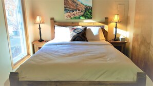 A neatly made bed with a wooden headboard, two bedside tables with lamps, and a painting above the headboard.