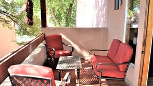 A balcony with red chairs and a table, overlooking a garden.