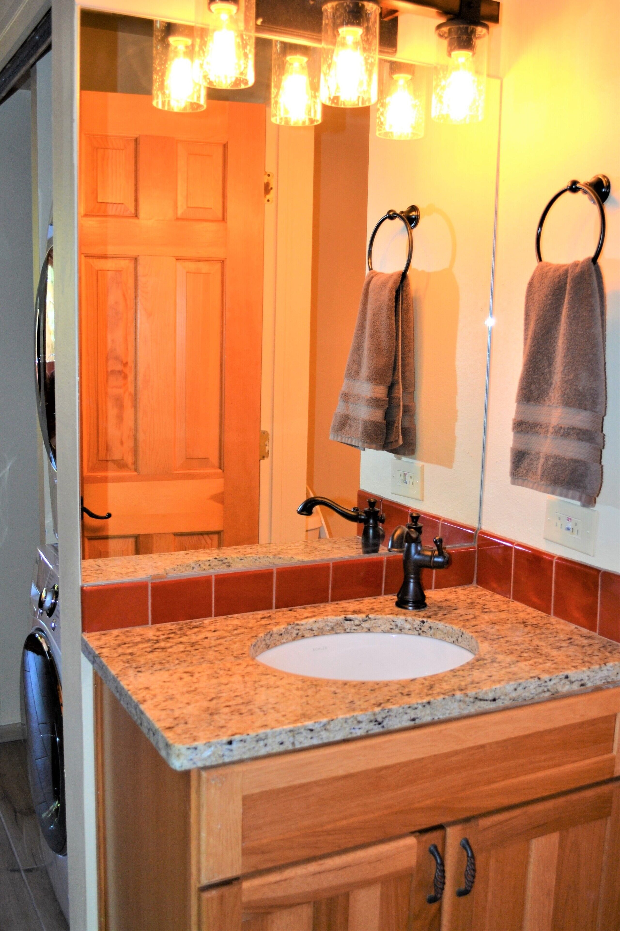 Une salle de bain avec un lavabo surmonté d’un plan de travail en granit, des meubles en bois, un miroir et un porte-serviettes.