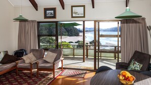 A room with a view of a beach and ocean, furnished with a sofa, chairs, and a table with fruit. - Fantastic Family Holiday Home with Breathtaking Views over Hot Water Beach (Hot Water Beach)