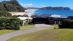 A coastal property with a driveway leading to a garage, surrounded by lush greenery and overlooking a beach and ocean. - Fantastic Family Holiday Home with Breathtaking Views over Hot Water Beach (Hot Water Beach)