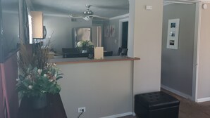 A room with a ceiling fan, a desk with a computer, a small black ottoman, and a potted plant.