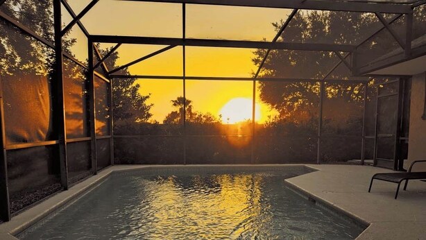 A swimming pool with a glass enclosure, surrounded by a patio area. - VERY CLEAN & SPACIOUS! Pool, Game Room, BBQ, 2 King Masters--Close to Disney! (Clermont)