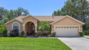 A single-story house with a beige facade, a front porch, a garage, and a well-maintained lawn. - VERY CLEAN & SPACIOUS! Pool, Game Room, BBQ, 2 King Masters--Close to Disney! (Clermont)